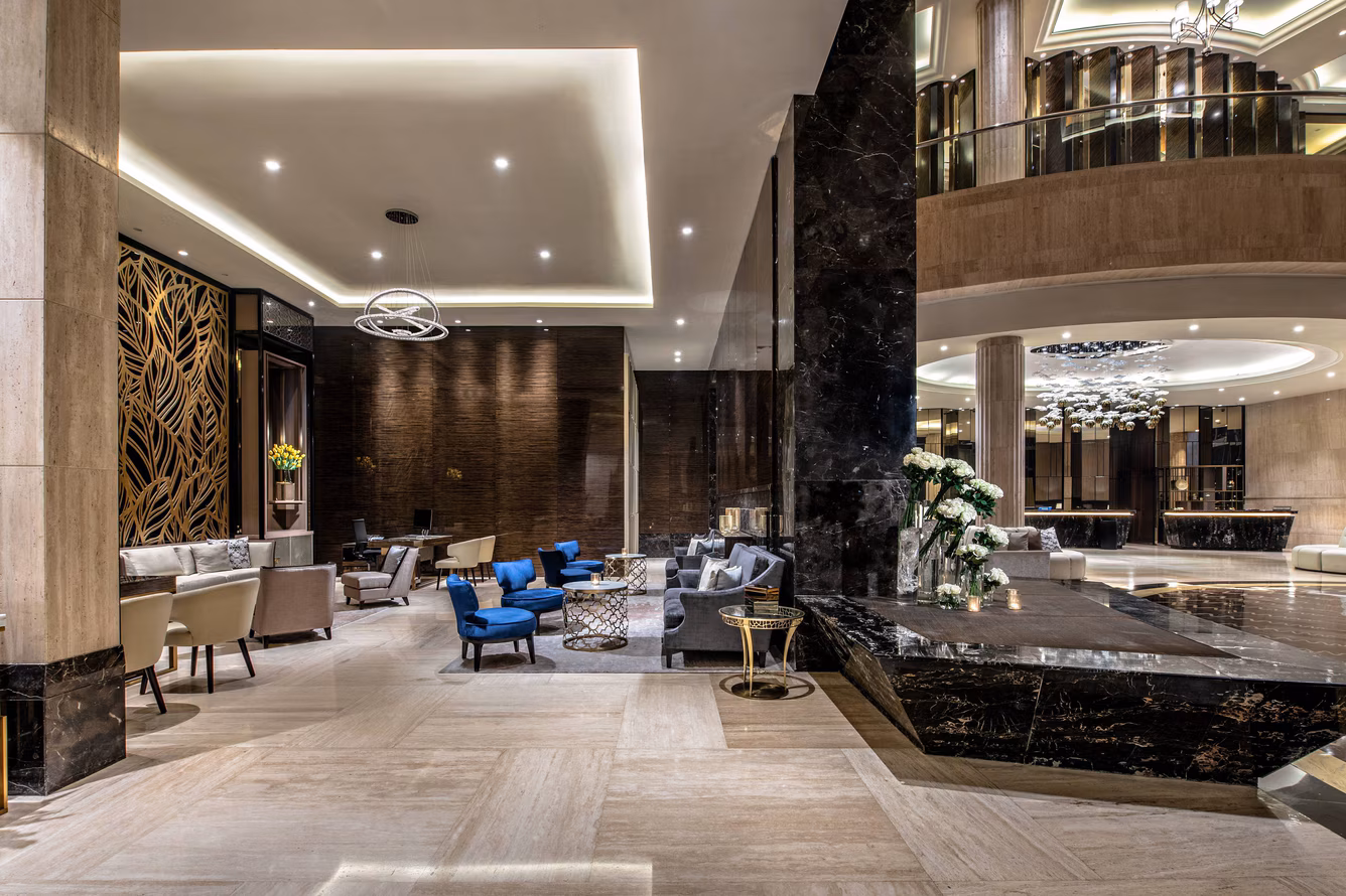 Desain interior lobi hotel mewah bernuansa modern dengan pilar marmer hitam, lampu gantung kristal, dan deretan kursi santai premium.