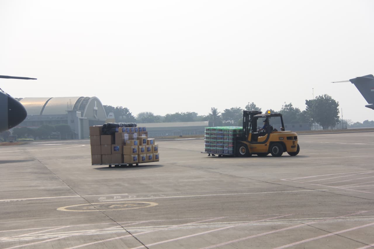 Kendaraan forklift mengangkut kardus berisi bantuan logistik di area posko penanggulangan bencana.
