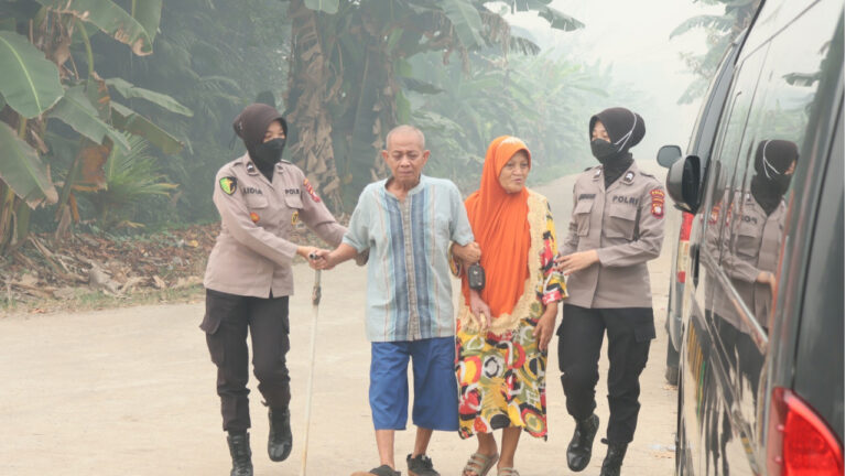 Dua anggota Polwan Polda Kalbar menuntun sepasang lansia di jalan terimbas kabut asap. (Dok. HO/Nusantara Post)