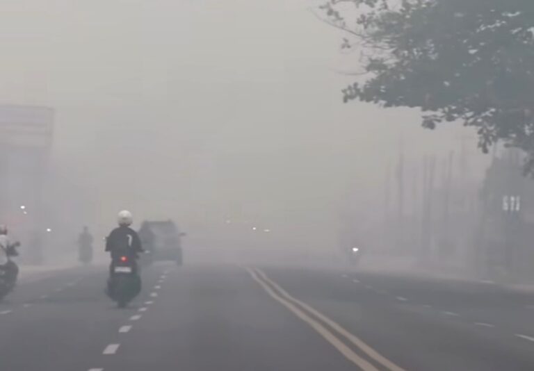 Pengendara sepeda motor dan mobil melintas di jalan raya yang tertutup kabut asap tebal sehingga jarak pandang pendek.