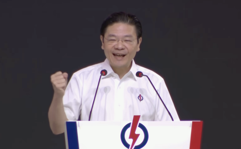 PM Singapura Lawrence Wong mengepalkan tangan saat memberikan pidato di mimbar berlogo petir.