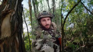 Prajurit Belarusian Volunteer Corps berhelm dan berkamuflase daun berbicara di depan kamera di hutan Ukraina. (Dok. Instagram/@belarusiancorps)