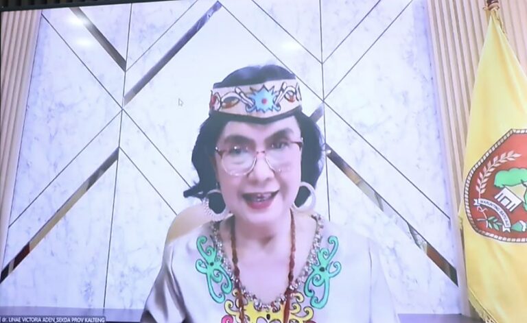 Sekda Kalteng Linae Victoria Aden tampil di layar monitor memberikan sambutan daring dengan bendera daerah di belakangnya.